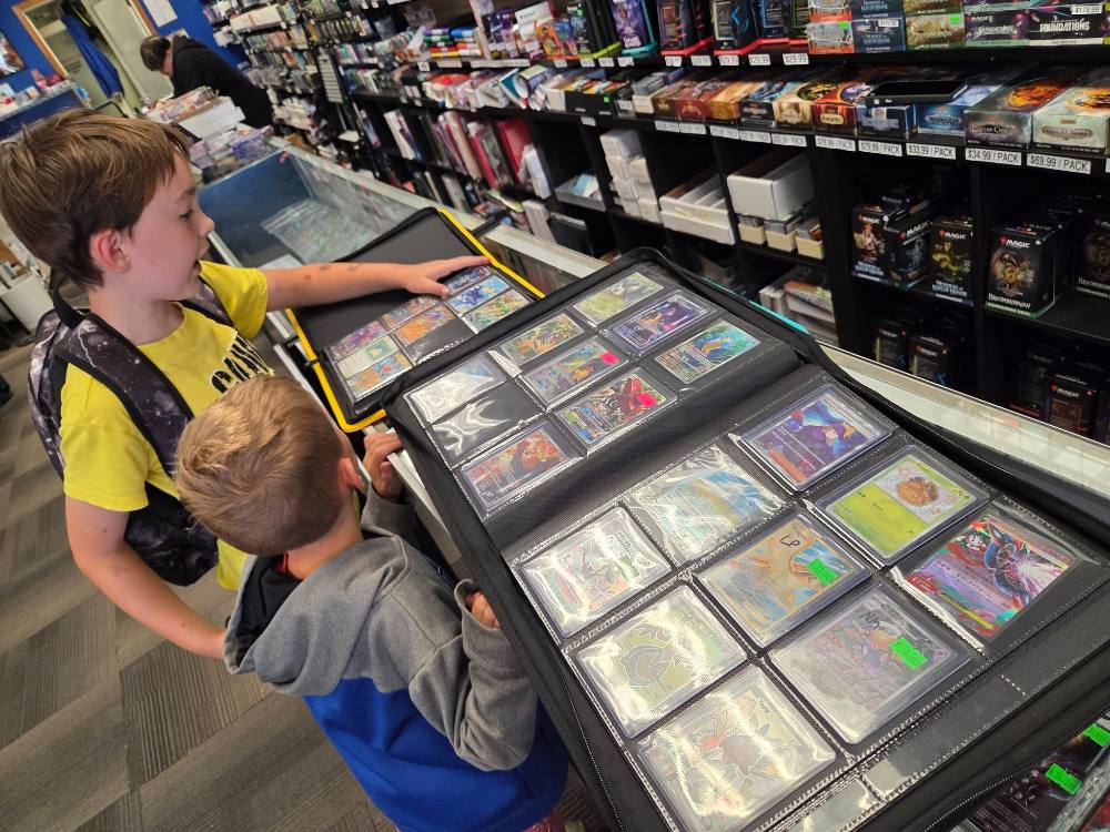 A kid in a yellow shirt looking through a binder of singles at the Cardtropolis counter